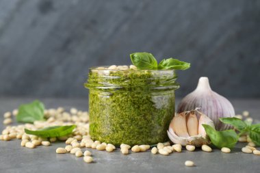 Kavanoz dolusu lezzetli pesto sosu ve malzemeler gri masada, yakın plan.