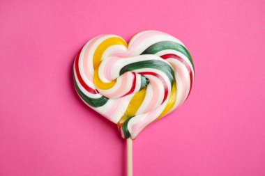 Pembe arka planda kalp şeklinde lolipopla kalın.
