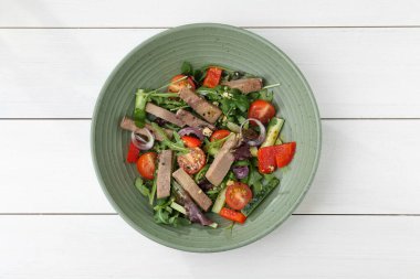 Biftek diliyle nefis bir salata ve beyaz ahşap masada sebzeler.