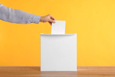 Oy sandığına oy veren kadın, tahta masada turuncu arka planda, yakın planda.