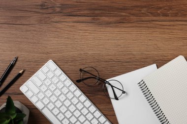 Merkez ofis. Bilgisayar klavyesi, gözlükler, ev bitkisi ve ahşap masadaki kırtasiye malzemesi, düz yatak. Metin için boşluk
