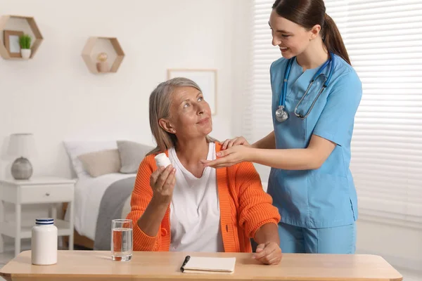 Young healthcare worker consulting senior woman at wooden table indoors