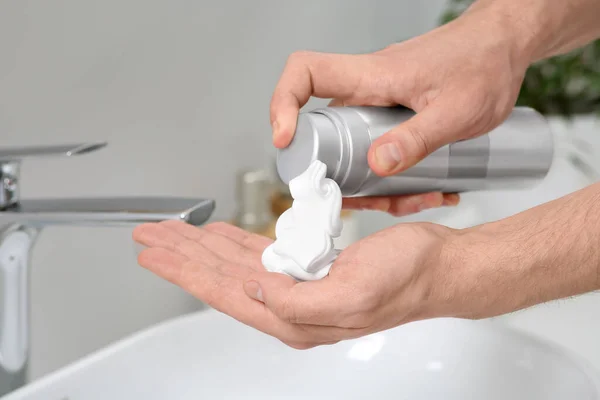Man applying shaving foam onto hand in bathroom, closeup