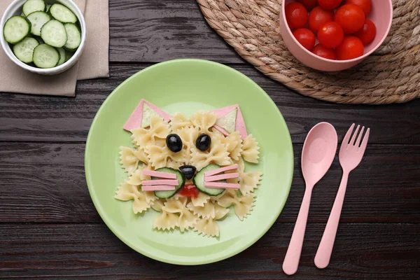 Creative serving for kids. Plate with cute cat made of tasty pasta, vegetables and sausage on wooden table, flat lay