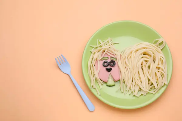 Creative serving for kids. Plate with cute dog made of tasty pasta, sausage and cucumber on pale orange table, flat lay. Space for text