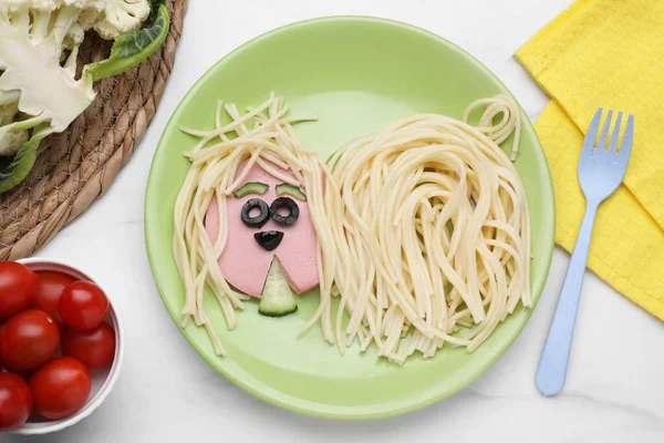 Creative serving for kids. Plate with cute dog made of tasty pasta, sausage and cucumber on white marble table, flat lay