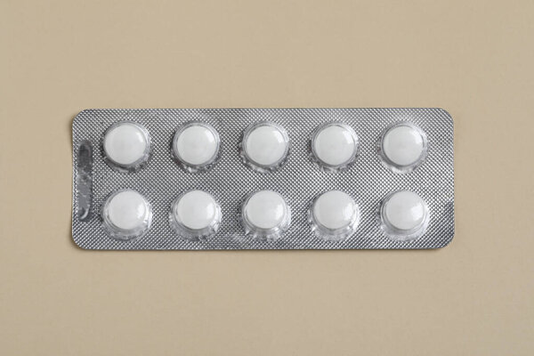 White pills in blister on beige background, top view