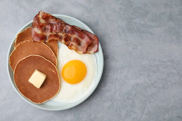 Tasty pancakes with fried egg and bacon on grey table, top view. Space for text