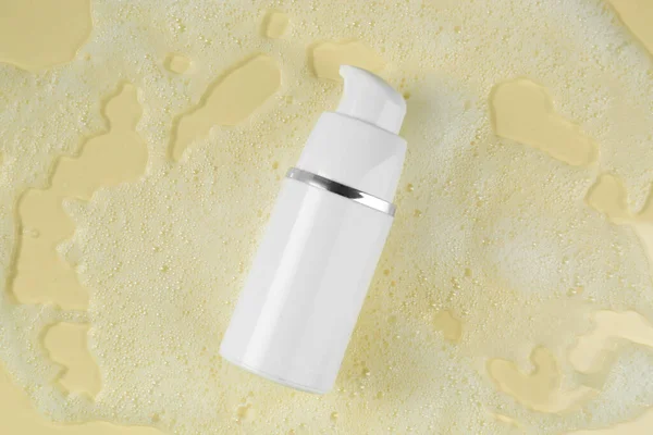 Bottle of face cleanser and white foam on beige background, top view. Skin care cosmetic