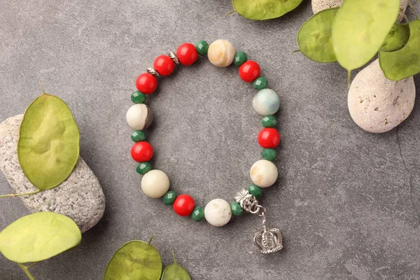 Beautiful bracelet with gemstones, leaves and stones on grey background, flat lay