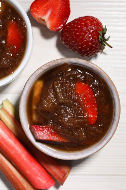 Lezzetli rhubarb reçeli kaselerde, saplar ve çilekler beyaz ahşap masada, düz yatıyordu.