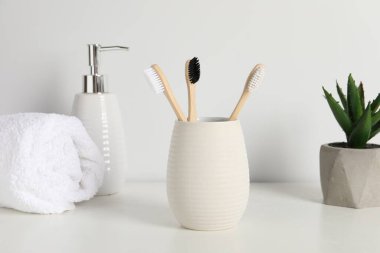 Bambu diş fırçaları kabın içinde, saksı bitkisi, havlu ve kozmetik ürünler beyaz tezgahın üzerinde