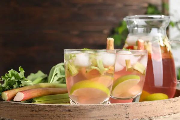 Tasty rhubarb cocktail with citrus fruits and stems on wooden board, closeup