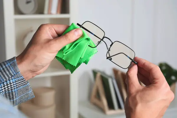 Man wiping glasses with microfiber cloth indoors, closeup