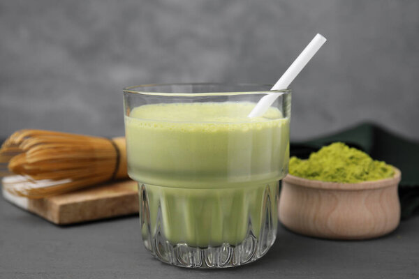 Glass of tasty matcha smoothie, powder and whisk on grey table, closeup