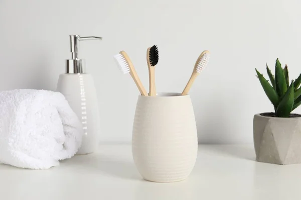 Bamboo toothbrushes in holder, potted plant, towel and cosmetic product on white countertop