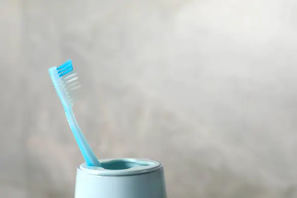 Plastic toothbrush in holder on light grey background, closeup. Space for text