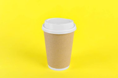Sarı arka planda plastik kapaklı kağıt bardak. Kahve hazır.
