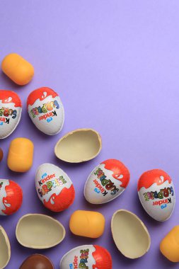 Sveti Vlas, Bulgaristan - 29 Haziran 2023: Mor arka planda Kinder Sürpriz Yumurtalar ve plastik kapsüller, düz konum. Metin için boşluk