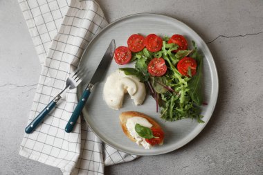 Lezzetli burrata peyniri domatesli, roka ve tost gri masada servis edilir.