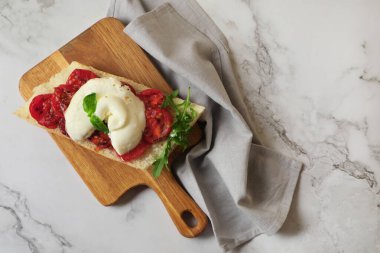 Toast with delicious burrata cheese, tomatoes and arugula on white marble table, top view. Space for text