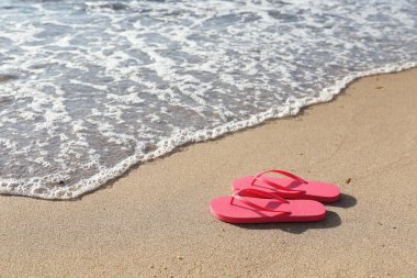 Deniz kenarındaki kumda pembe parlak parmak arası terlikler. Metin için boşluk
