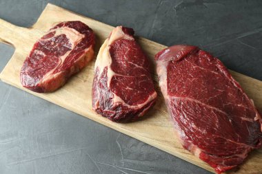 Gri masada çiğ et parçaları olan ahşap tahta.