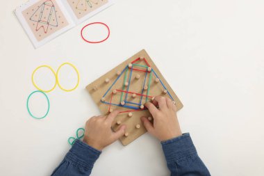 Motor beceri geliştirme. Çocuk beyaz masada coğrafya ve lastik bantlarla oynuyor.