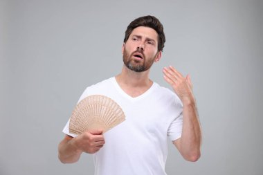 Elinde yelpaze olan mutsuz bir adam açık gri arka planda sıcaktan muzdarip.