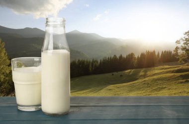 Bardaktaki taze süt ve ahşap masadaki şişe dağ manzarasına karşı, metin için yer.