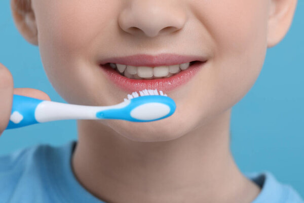 Girl brushing her teeth with toothbrush on light blue background, closeup