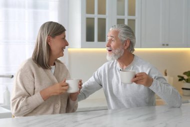 Mutfaktaki beyaz mermer masada bir bardak içkili sevimli yaşlı çift.