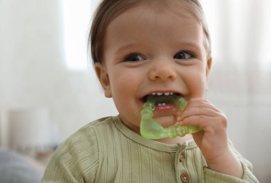 Evinde diş çıkarma oyuncağı olan sevimli bir kız bebek, yakın plan.