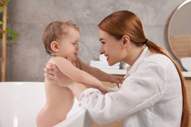 Anne küçük bebeğini küvette yıkıyor.