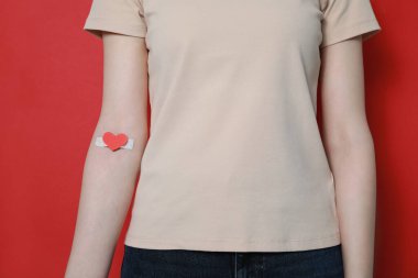 Kan bağışı konsepti. Kolunda kırmızı arka planda yapıştırıcı olan kadın, yakın plan.