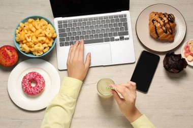 Kötü yeme alışkanlıkları. Bir bardak içkisi ve aperatifleri olan bir kadın tahta masada dizüstü bilgisayar kullanıyor.