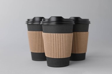 Açık gri arka planda siyah kapaklı kağıt bardaklar. Kahve hazır.