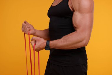 Turuncu arka planda elastik direniş bandıyla egzersiz yapan genç adam, yakın plan.