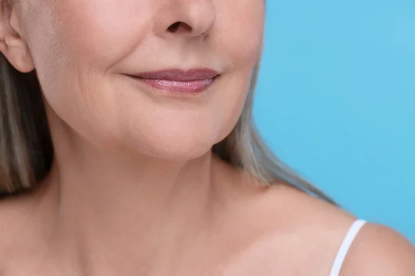 Senior woman with aging skin on light blue background, closeup. Rejuvenation treatment