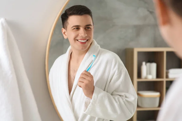 Happy man with toothbrush near mirror in bathroom