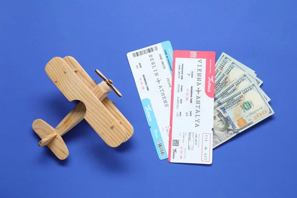 Dollars, wooden model of plane and tickets on blue table, flat lay. Business trip