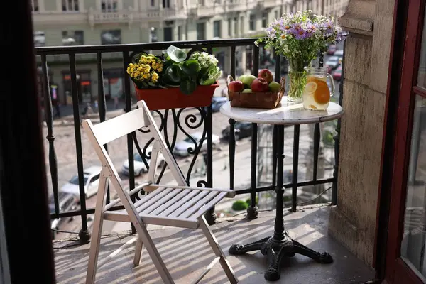 Relaxing atmosphere. Refreshing drink, apples and beautiful flowers on table near potted houseplants at balcony