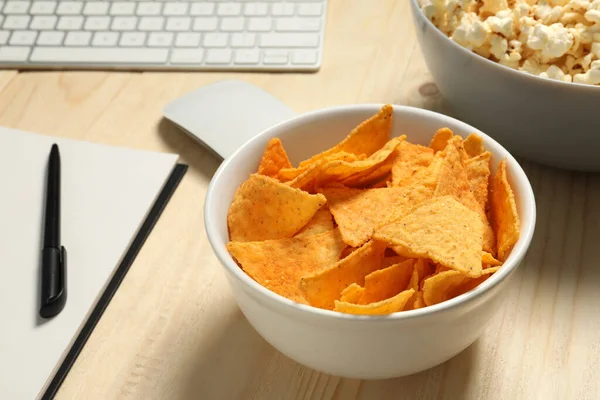 Bad eating habits at workplace. Tasty tortilla chips in bowl on wooden table, closeup