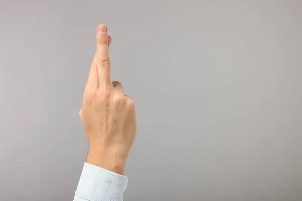 Man crossing his fingers on grey background, closeup. Space for text