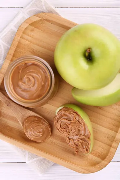 Fresh green apples with peanut butter on white wooden table, top view