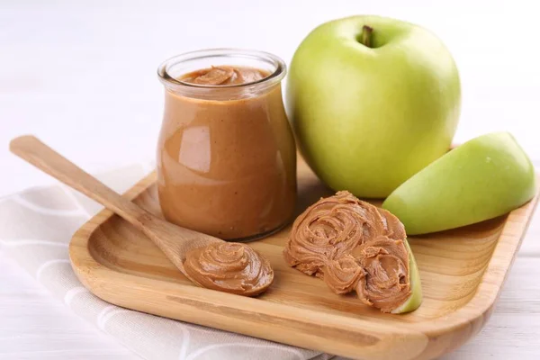 Fresh green apples with peanut butter on white wooden table