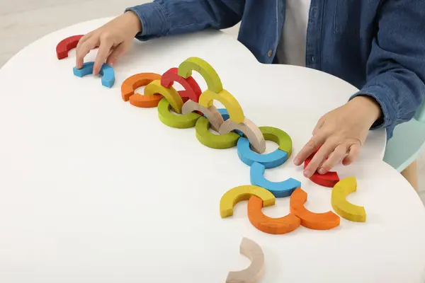 Motor skills development. Boy playing with colorful wooden arcs at white table, closeup