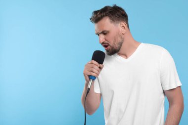 Mikrofonlu yakışıklı adam açık mavi arka planda şarkı söylüyor. Metin için boşluk