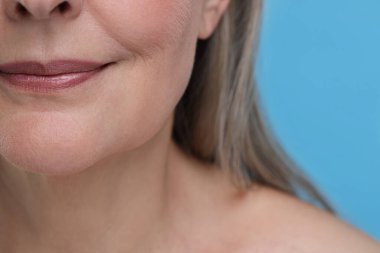 Açık mavi arka planda yaşlanan yaşlı bir kadın, yakın plan. Yenilenme tedavisi