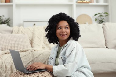 Pouf 'un evinde dizüstü bilgisayar kullanan mutlu genç bir kadın.